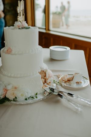 An elegant three-tier white wedding cake decorated with delicate pink flowers and pearled details.