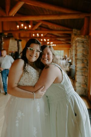 Two people in white dresses share a joyful embrace at a wedding celebration.