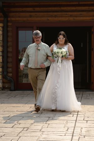 A bride in a flowing white gown walks along a stone pathway during her wedding ceremony.