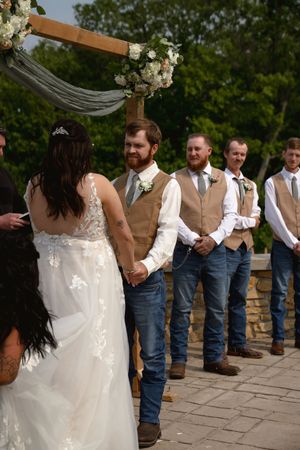 A wedding party lines up under a floral-decorated wooden arch during an outdoor ceremony.