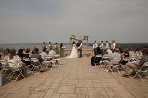 An outdoor wedding ceremony setup with white chairs and wooden arch against a scenic lake backdrop.