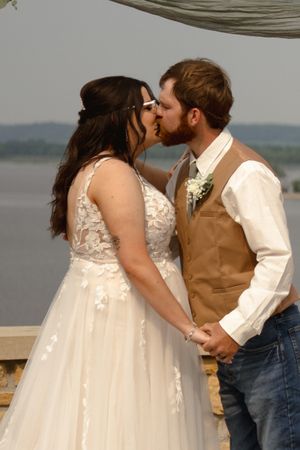 A romantic wedding kiss captured at an outdoor venue overlooking a scenic lake view.