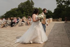 A bride in a flowing white dress holds her bouquet during an outdoor wedding ceremony.