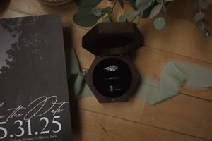 A wedding ring box and save the date card arranged with eucalyptus leaves.