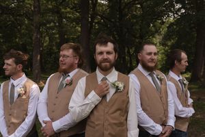 Groomsmen in matching tan vests and white shirts pose in a wooded setting.