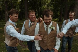 Groomsmen in matching tan vests share a lighthearted moment during wedding photos.