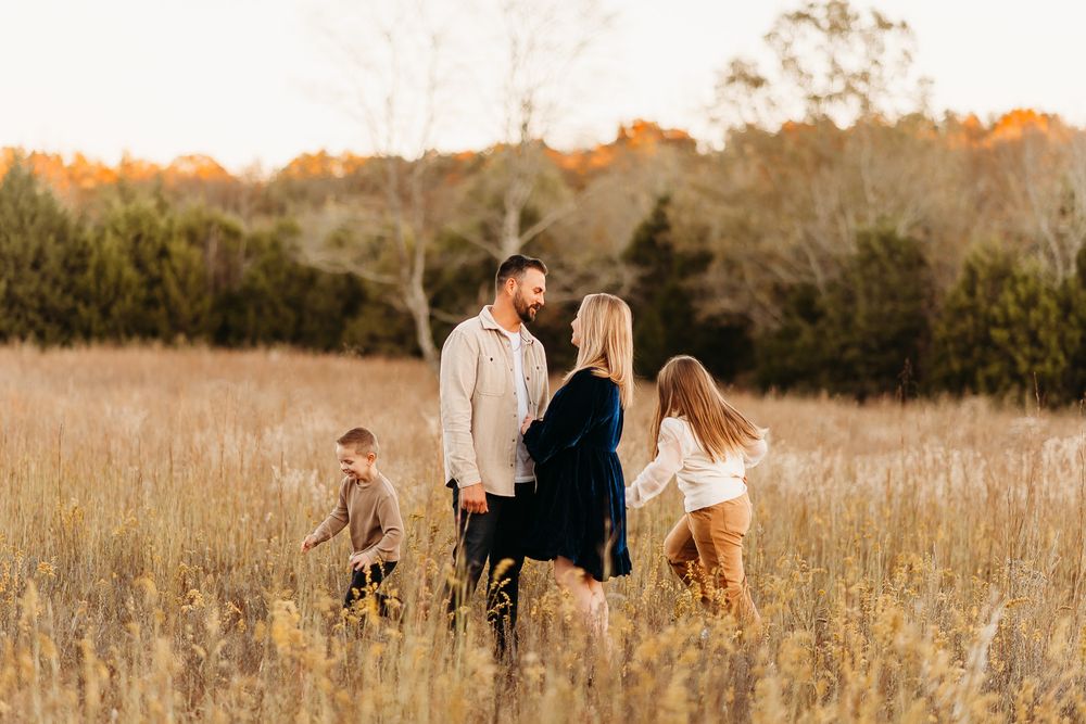 A family stands together in a golden field with tall grass during sunset while wearing casual attire.