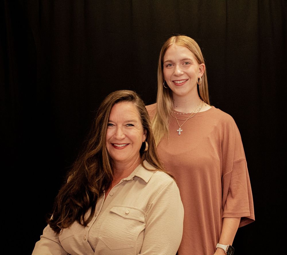 Two women in neutral-toned clothing smile while posing together for a casual photo.