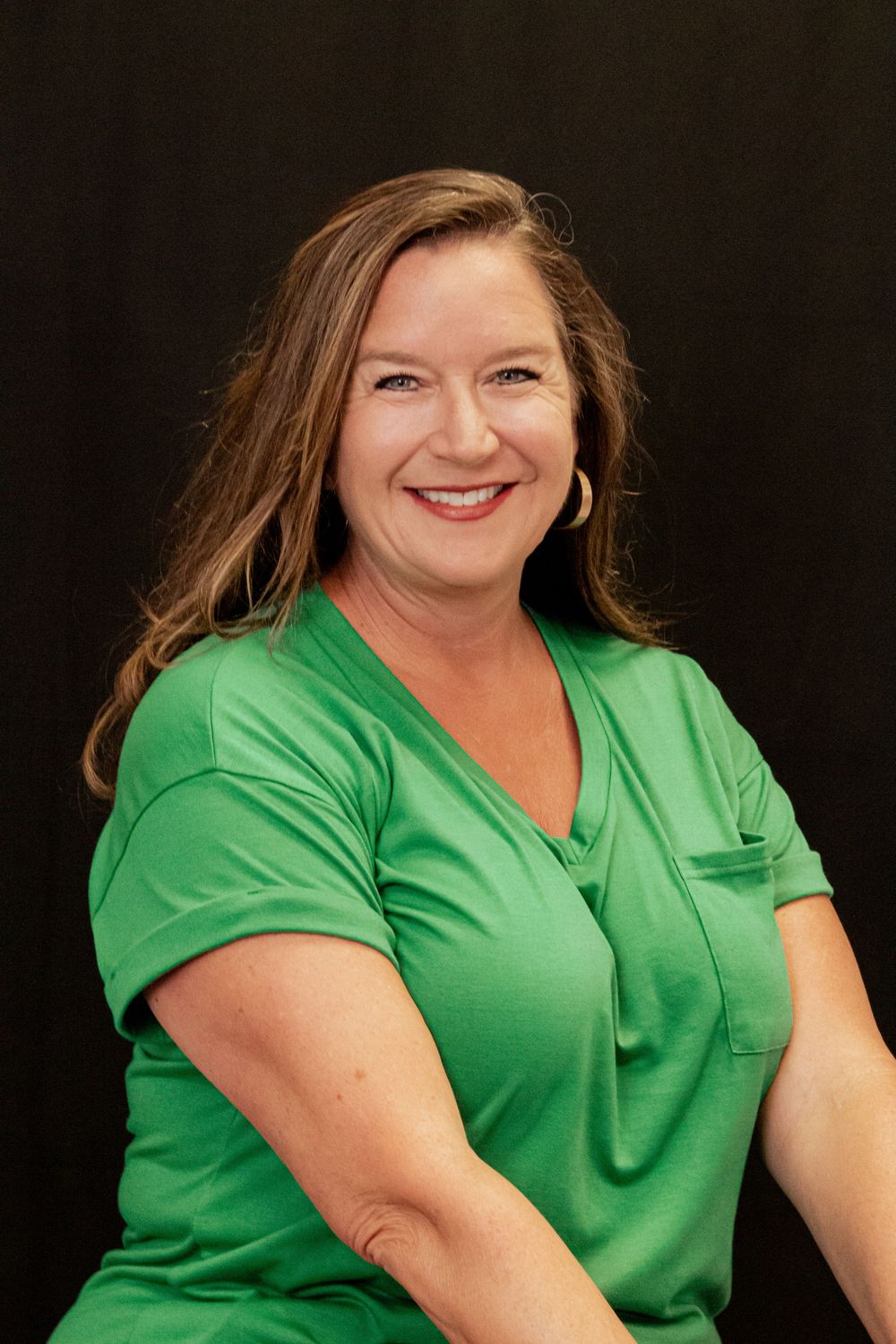 Professional headshot portrait of someone in a bright green v-neck top against a dark background.