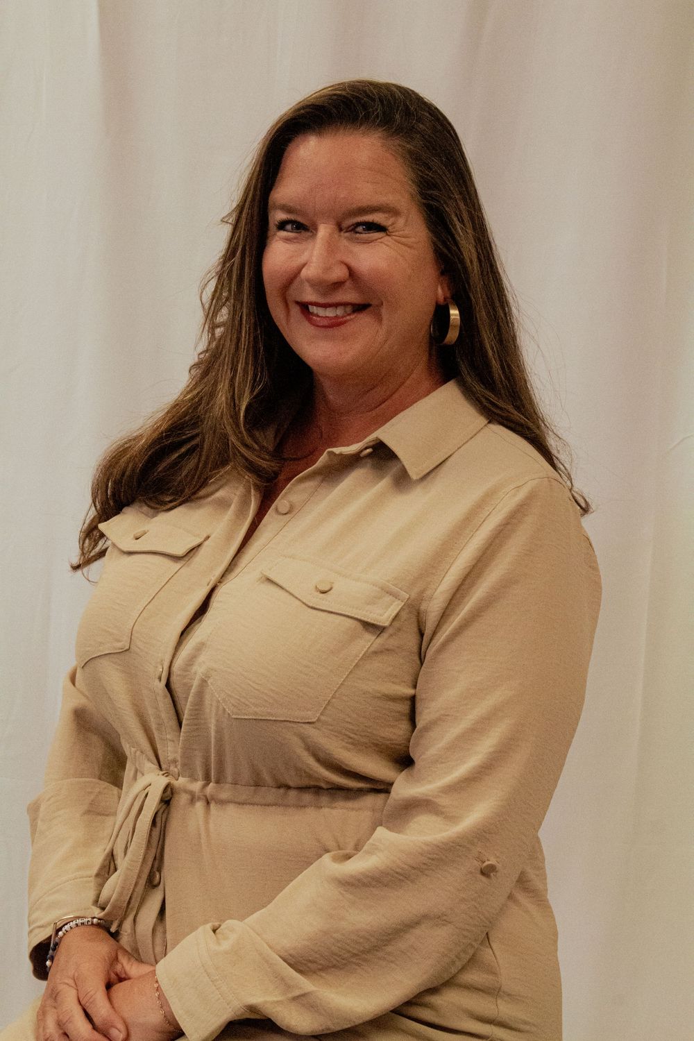 Professional portrait of someone wearing a beige belted dress with pockets and collar against a light background.