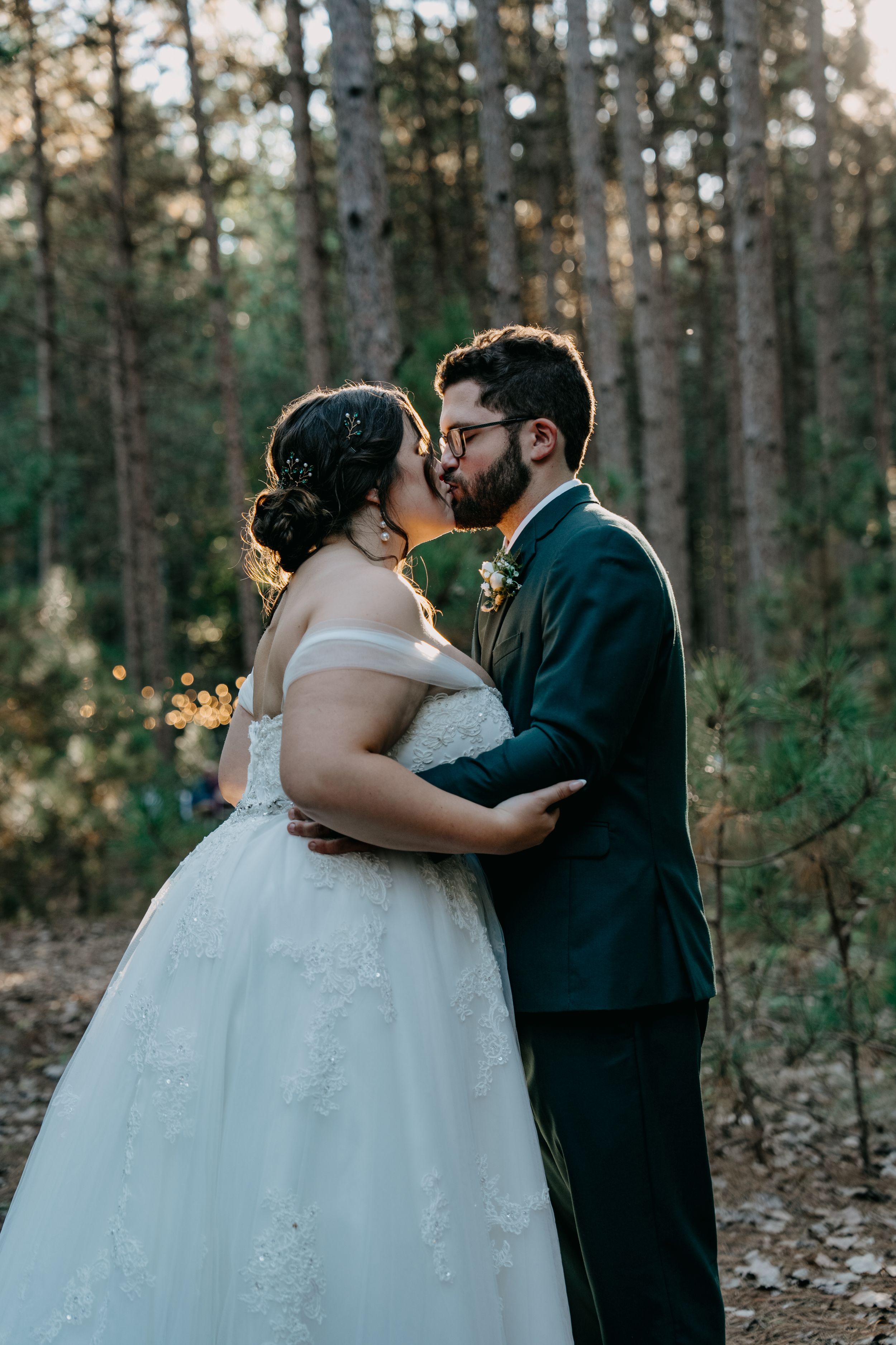 A romantic wedding photo of a couple sharing a tender kiss in a sunlit forest setting.