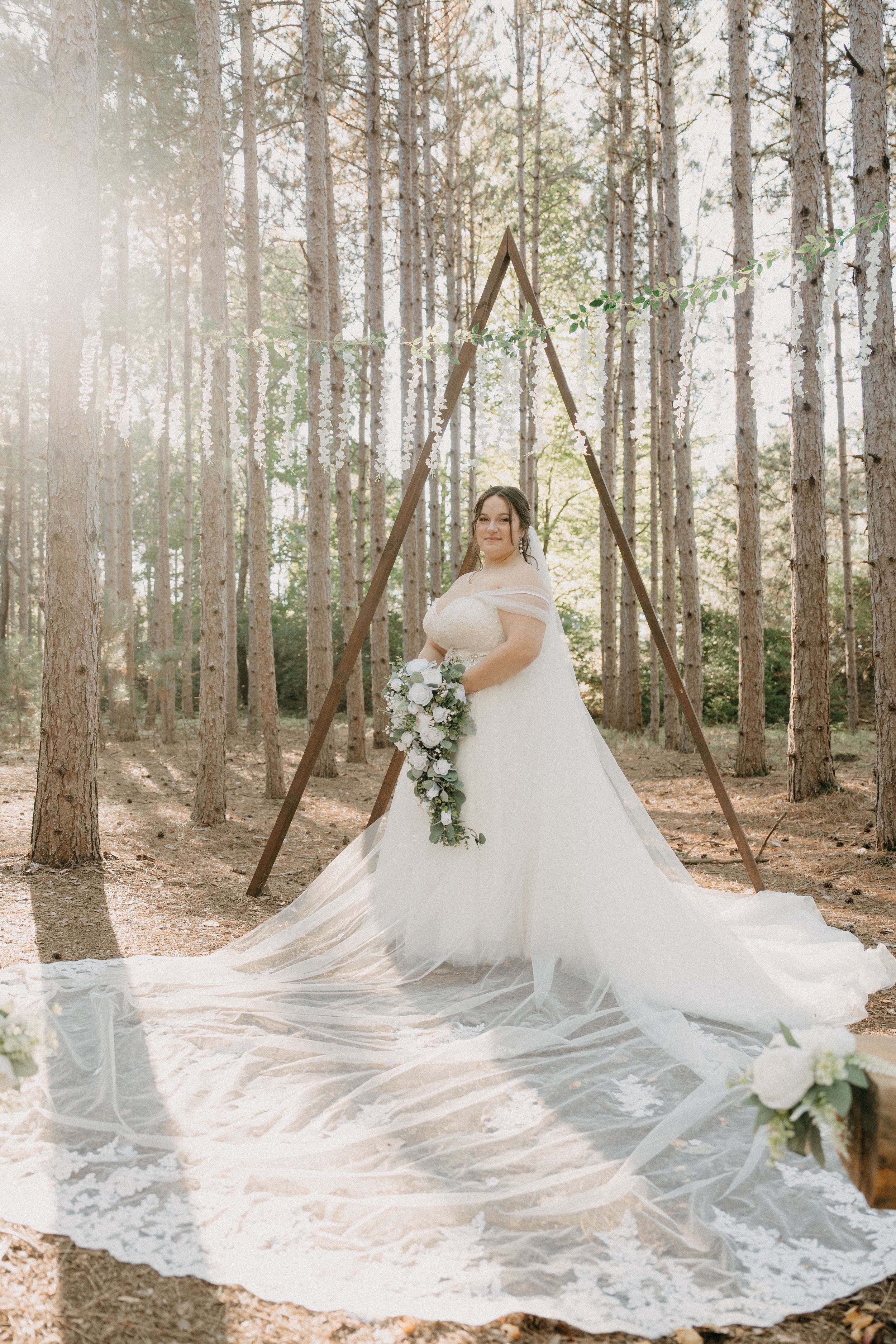 A dreamy wedding portrait features an elegant off-shoulder gown with flowing train in a sunlit pine forest.