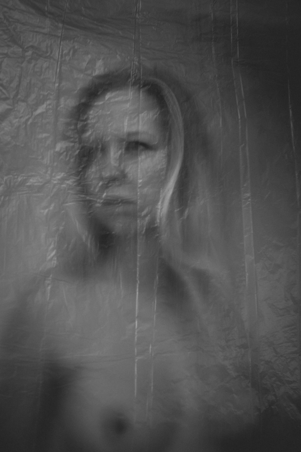 Black and white artistic portrait with ethereal blurred effect showing a ghostly figure behind textured surface.