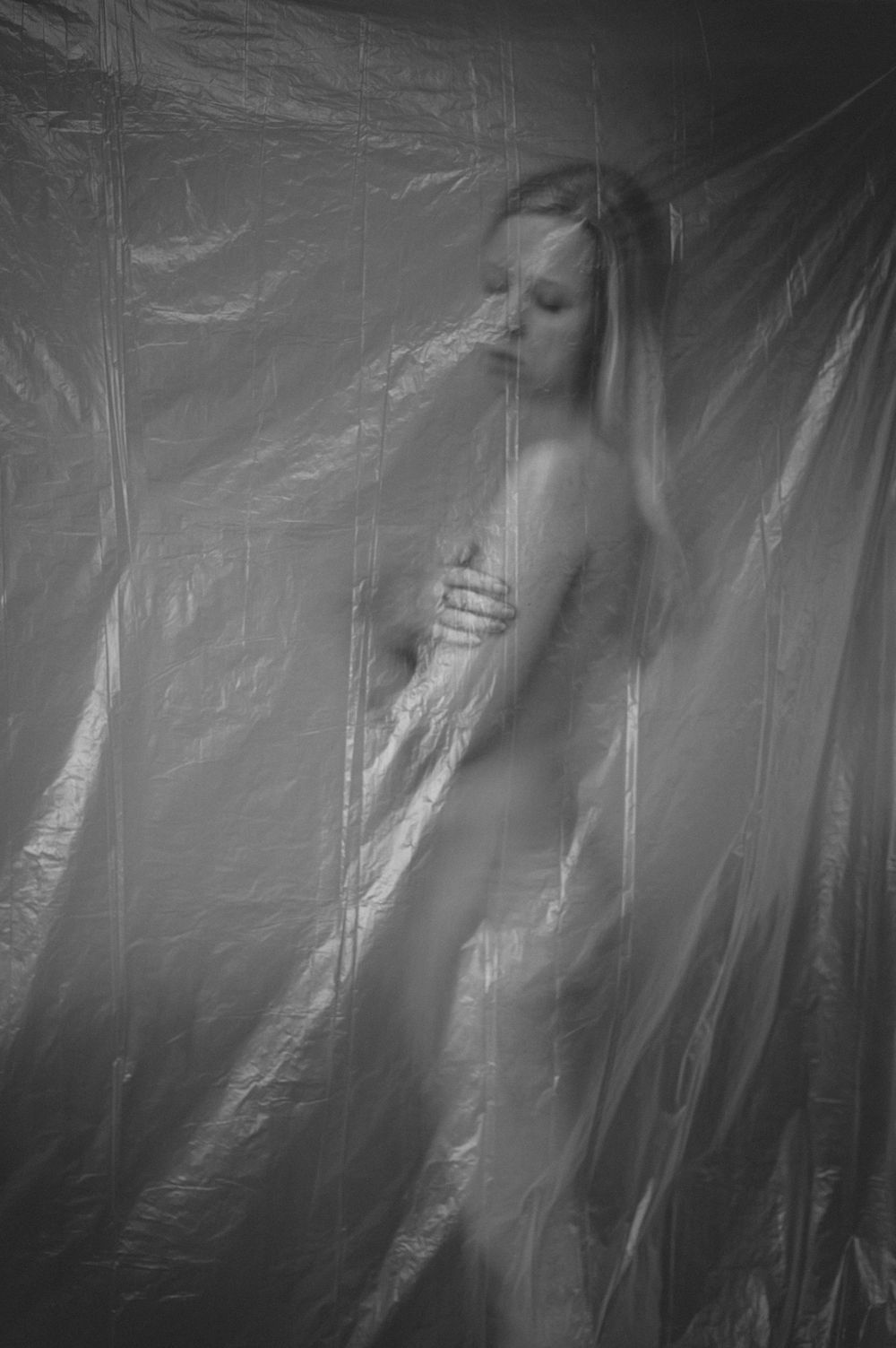Artistic black and white photograph of ethereal figure behind translucent fabric creating a dreamy silhouette effect.