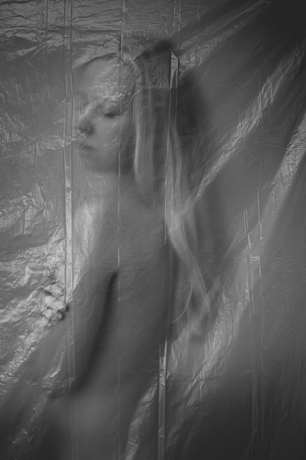 Abstract black and white artistic photograph showing draped fabric with light and shadows creating ethereal shapes through wrinkles.