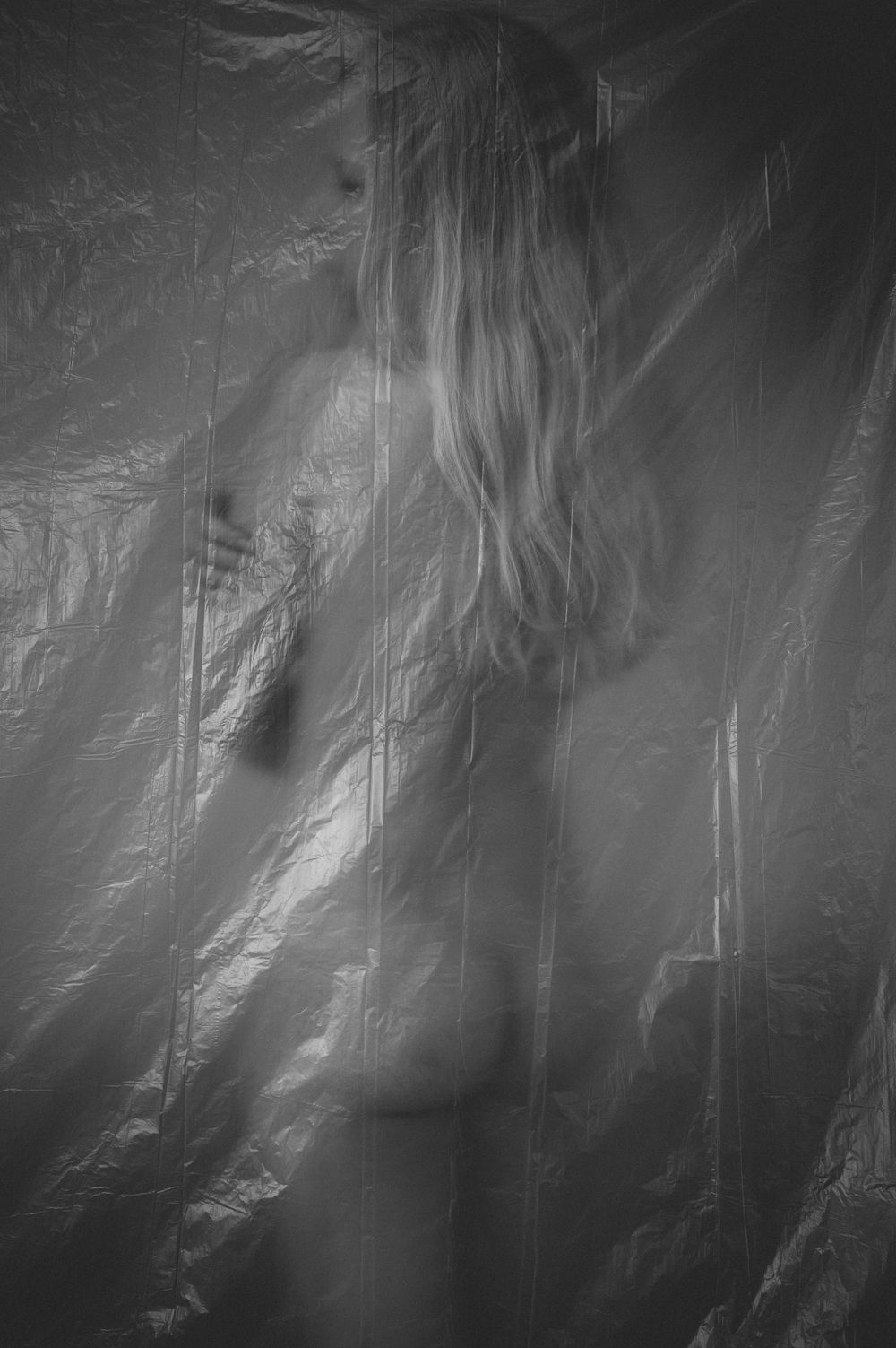 Abstract black and white artistic photograph showing ethereal silhouette behind textured, translucent material creating moody effect.