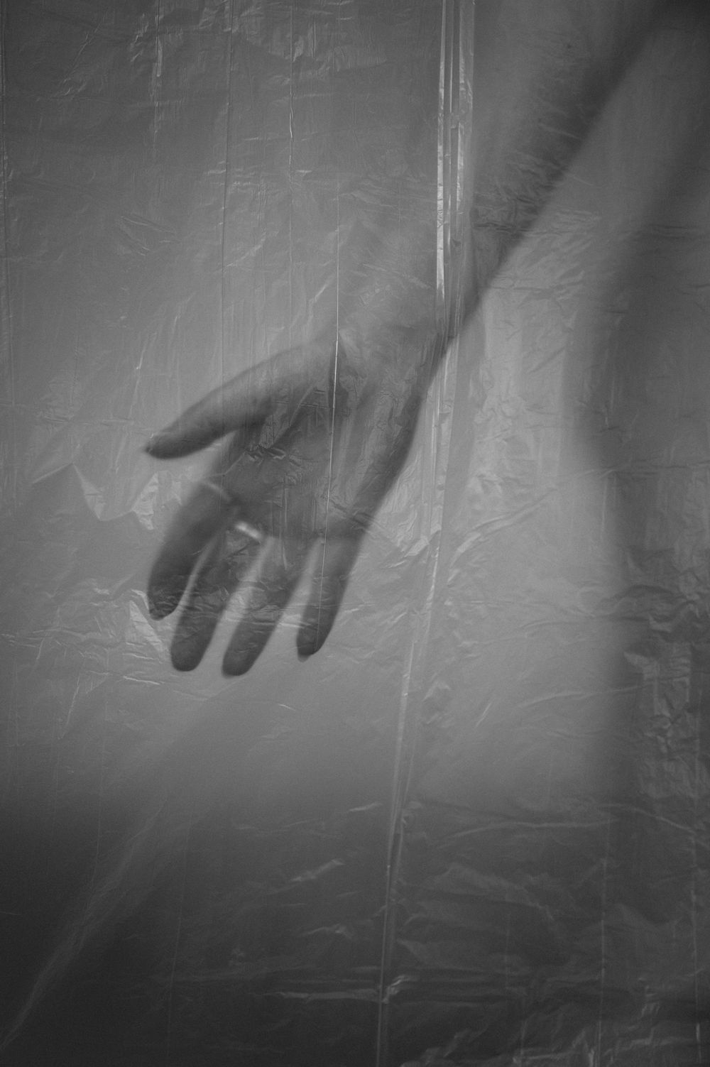 A haunting black and white image of a hand reaching through a translucent fabric creating an ethereal silhouette.
