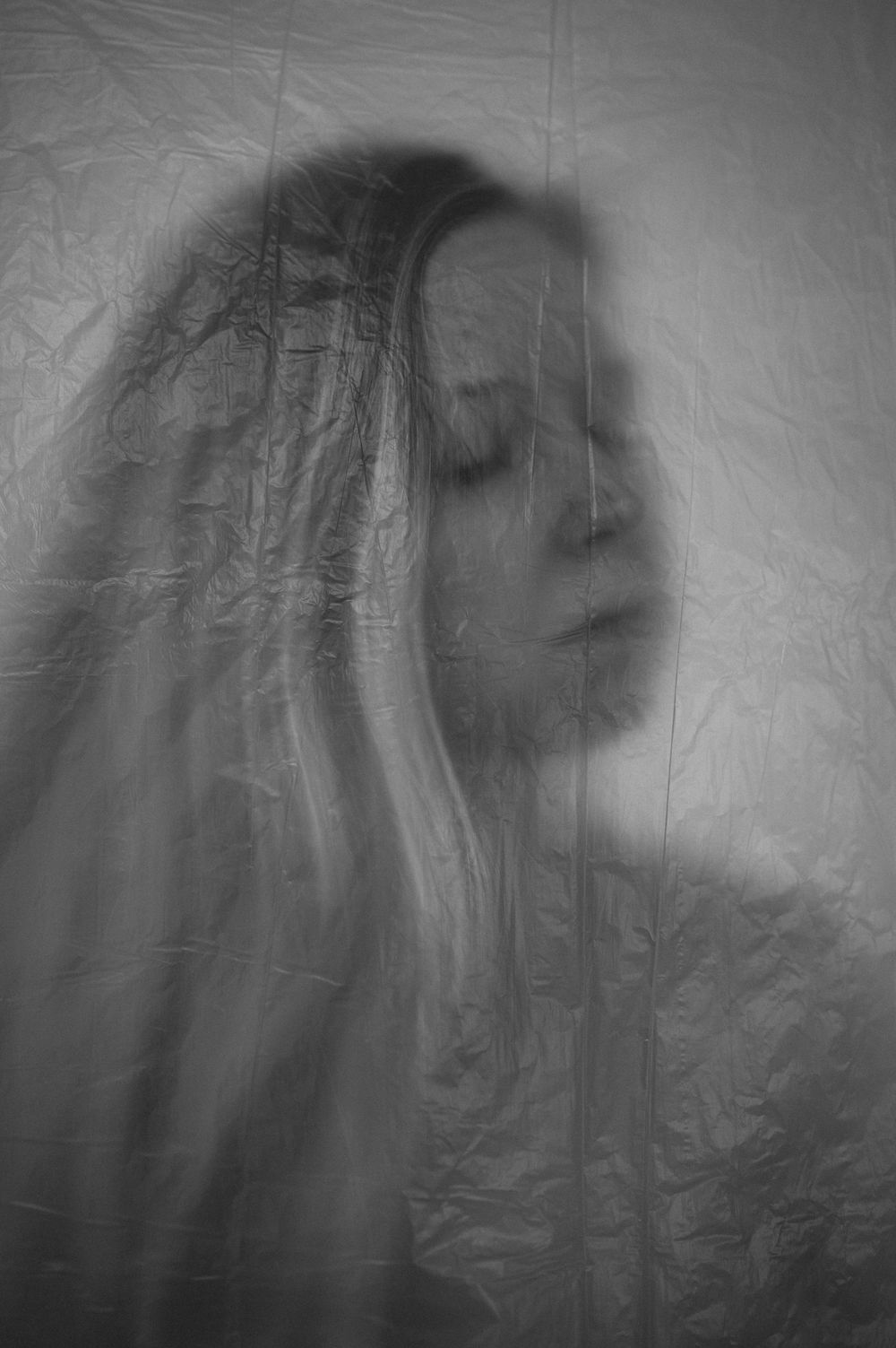 Ethereal black and white portrait through textured fabric creates a dreamy, ghostlike effect with soft focus and flowing hair.