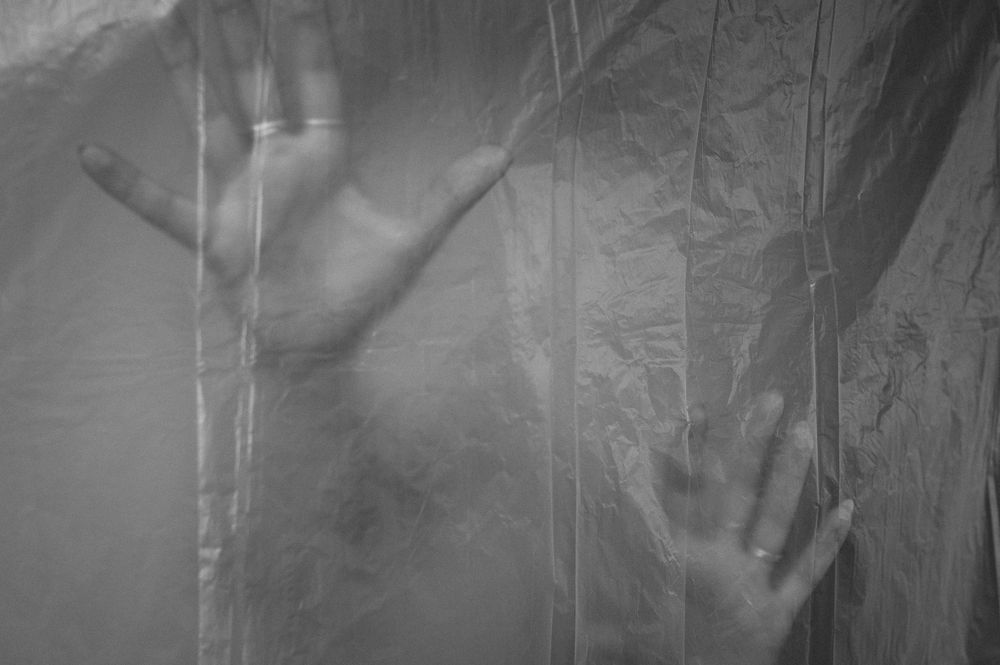 Silhouetted hands press against a translucent fabric creating an eerie and haunting effect in black and white.