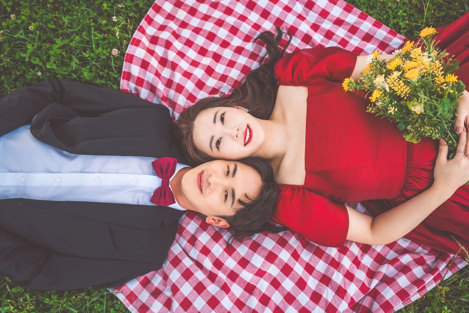 A couple relaxing on red checkered blanket with yellow flowers outdoors.
