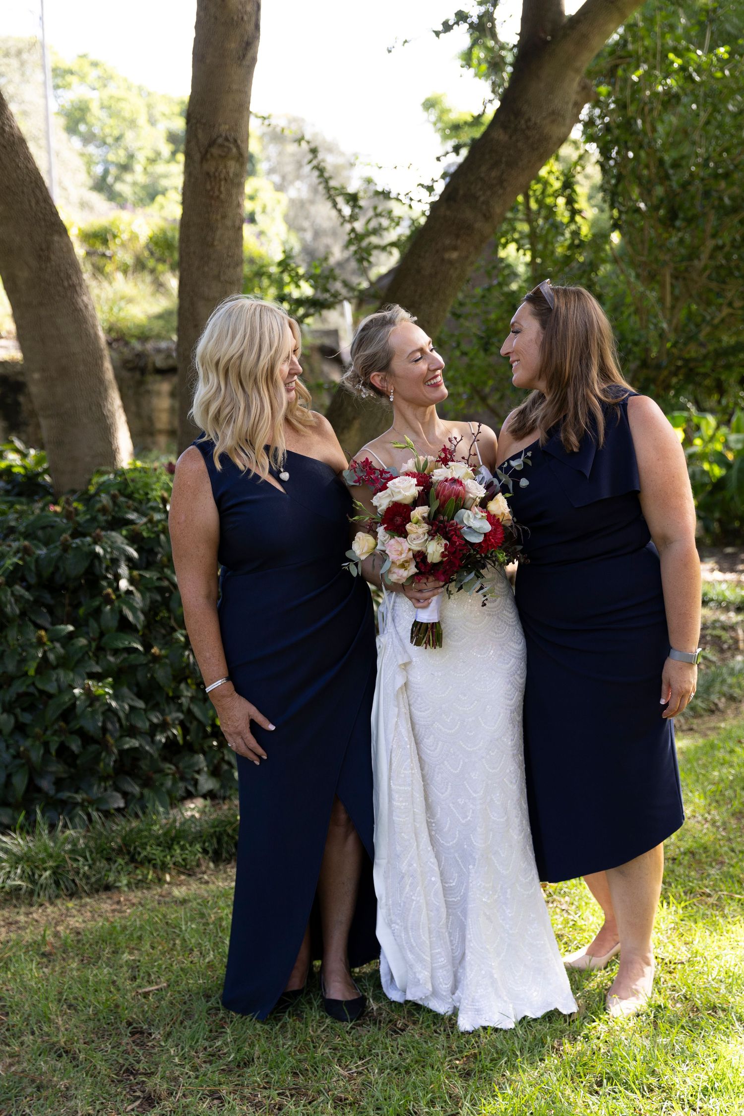 Wedding party wearing navy blue and white dresses sharing candid laughter outdoors in a garden setting.
