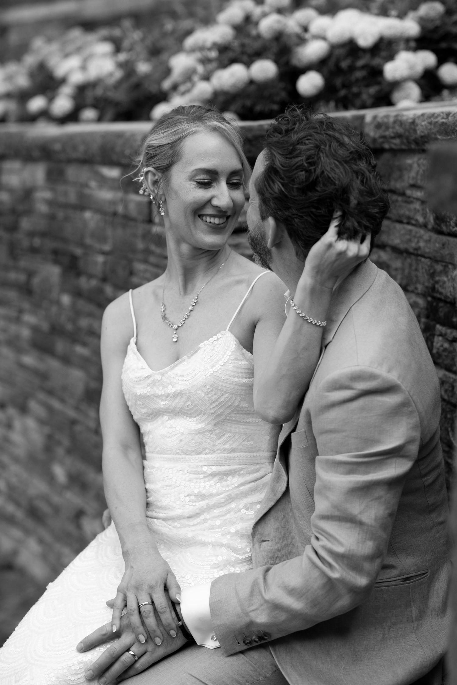 Black and white portrait of a bride and groom sharing an intimate moment against a brick wall.