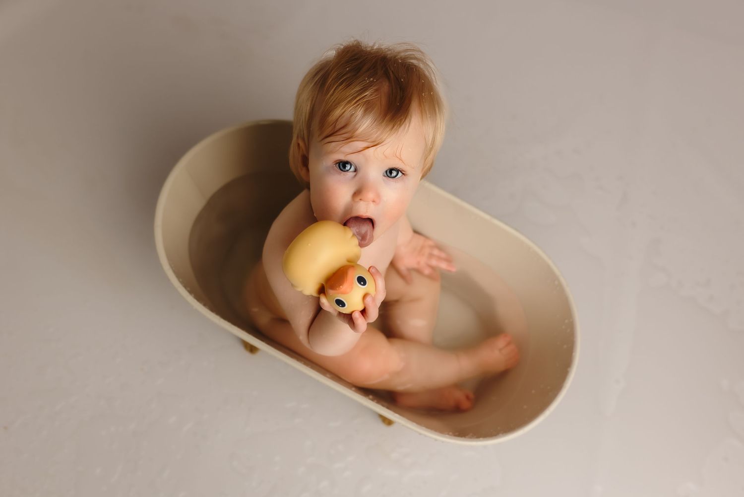 Smiling one-year-old girl in tub with rubber duck after cake smash at Somerset Portraits baby and newborn studio in Charlottesville.