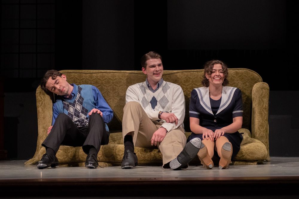 Performers lie on their backs on stage during a theatrical comedy scene.