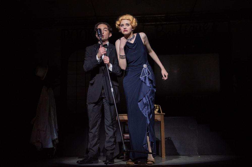 Performers in dark outfits strike dramatic poses during a stage production in atmospheric lighting.