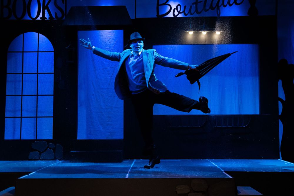 Ballet dancers perform a dramatic sequence in blue lighting on stage with window backdrops.