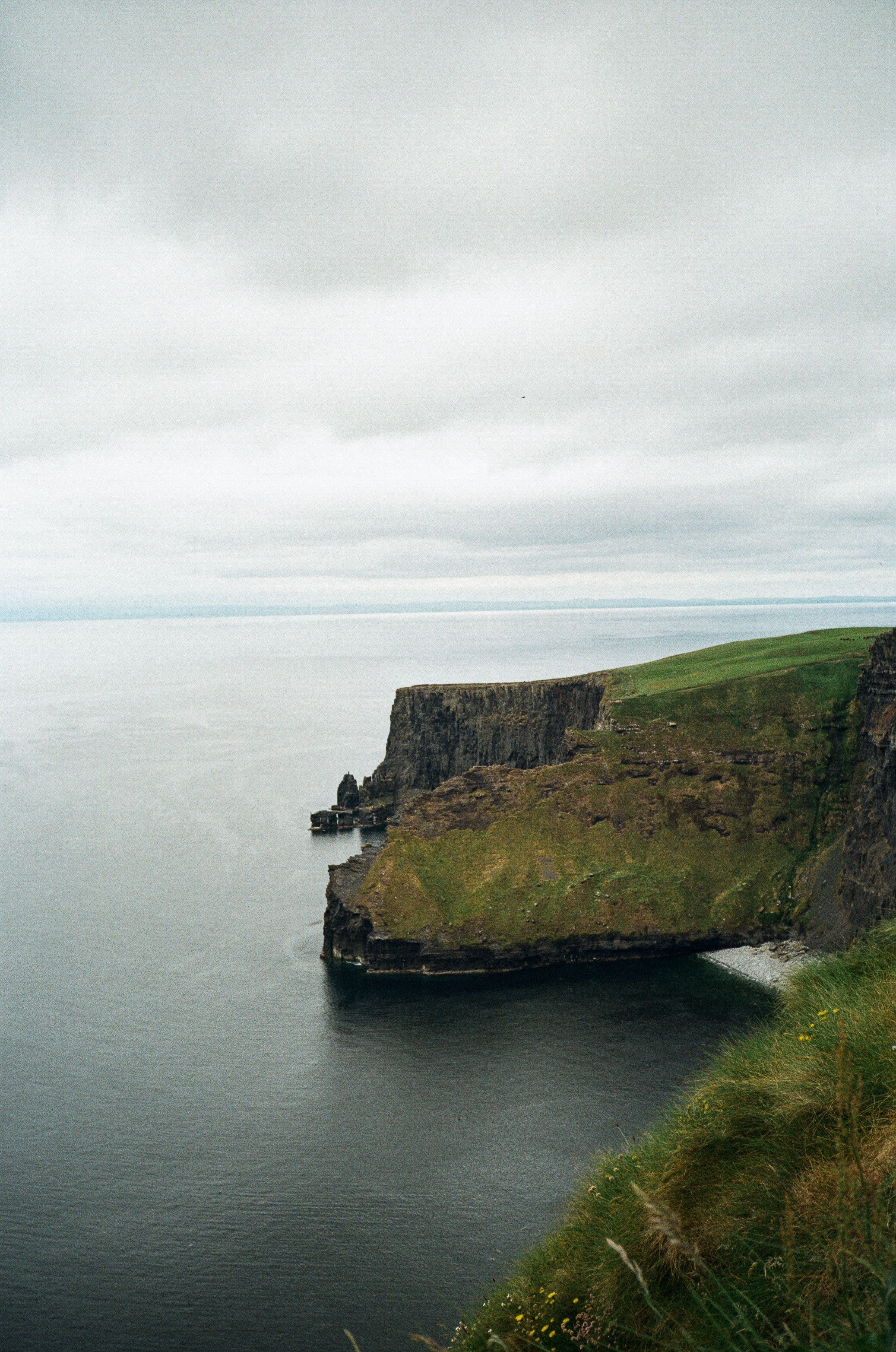 Dramatic coastal cliffs of the Cliffs of Moher rise above the Atlantic Ocean in Ireland under moody gray skies.