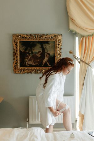 Sunlit bedroom interior with ornate classical artwork and peach curtains creating a romantic boudoir atmosphere.