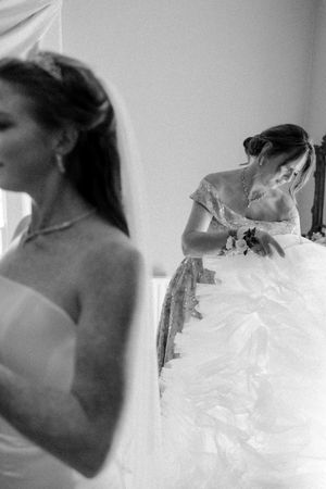 Black and white photo showing a bride getting ready in her wedding dress with another person in soft focus.