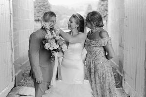 Black and white wedding photo of three people laughing and sharing a candid moment in a doorway.