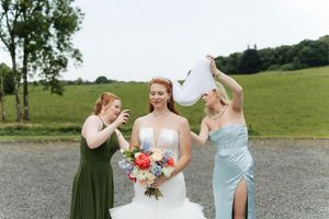 Bride in white gown poses with two bridesmaids in contrasting dresses against a countryside landscape.
