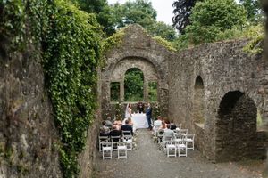 Outdoor wedding ceremony setup with white chairs arranged in old stone castle ruins covered in green ivy vines.
