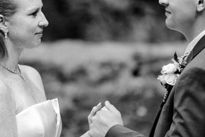Black and white close-up of bride and groom holding hands during intimate outdoor wedding ceremony.