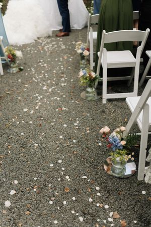 White flower petals scattered along the ground near white folding chairs at an outdoor event venue.
