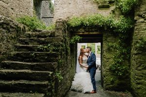 Two figures stand in a romantic stone archway framed by ancient stairs and lush green ivy at a historic venue.