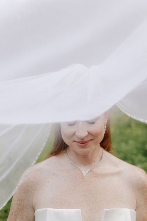 A close-up wedding photo shows a gentle smile under a flowing white veil against a soft green background.