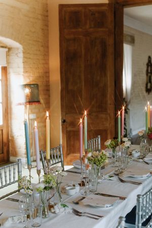 An elegant white wedding table setting with tall blue taper candles and small floral arrangements in glass vases.