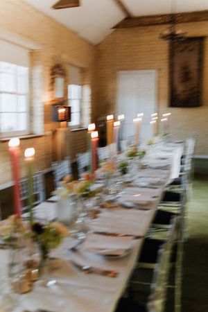 A long elegant dining table with tall red candles and place settings in a rustic room with natural lighting.