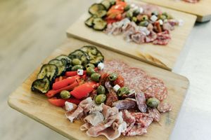 Fresh antipasto ingredients including cured meats, grilled zucchini, tomatoes and cheese arranged on wooden cutting boards.