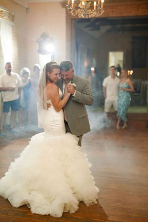 A father-daughter dance at a wedding reception with a stunning ruffled wedding dress in a chandelier-lit ballroom.