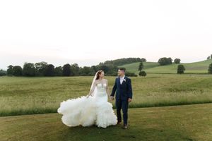 Newlyweds stand together on rolling green hills at a scenic outdoor wedding venue in the countryside.