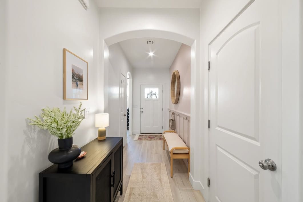 A bright modern entryway hallway with white walls, hardwood floors, black console table and decorative greenery.