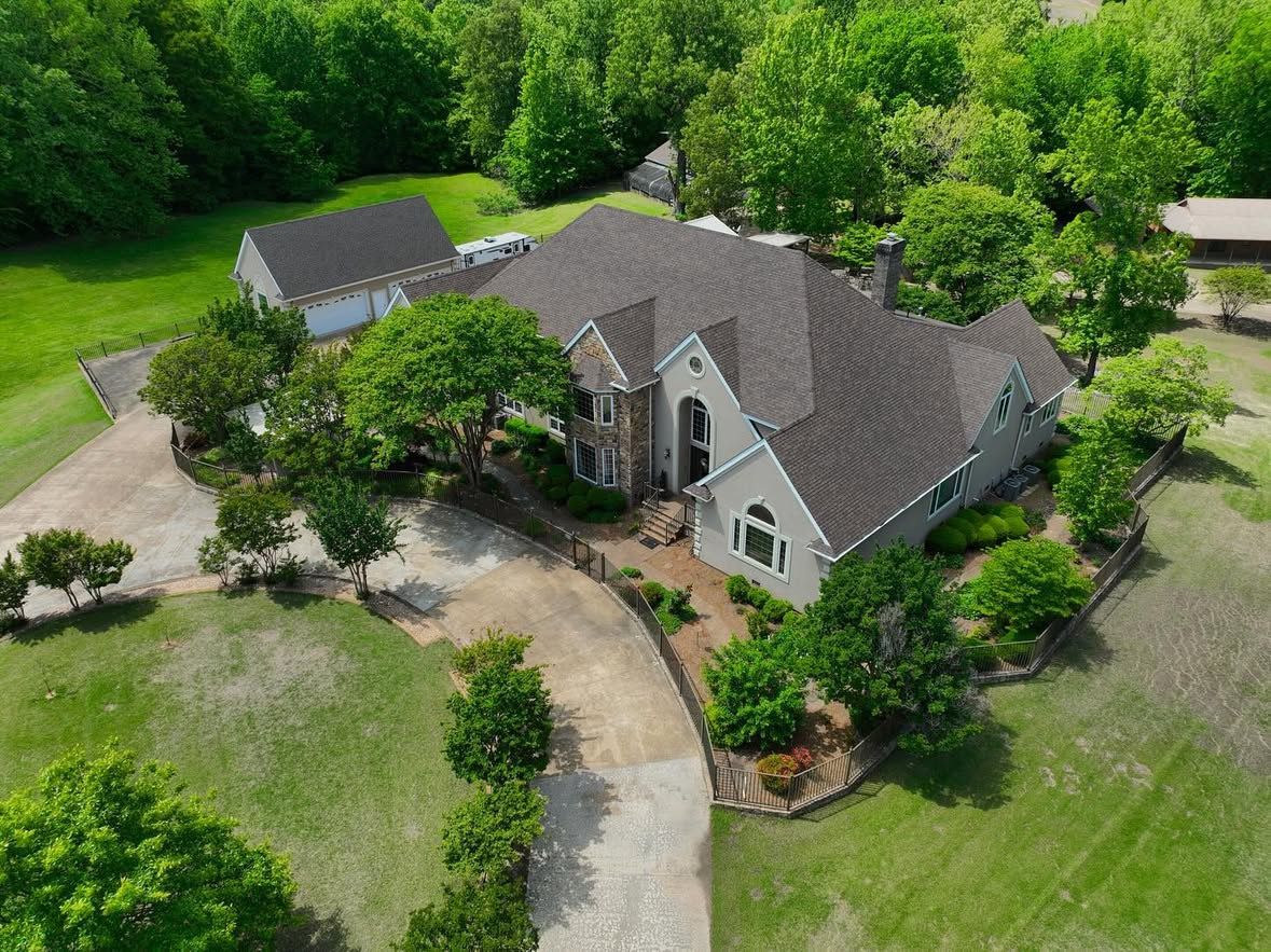 Aerial view of a lush residential property with multiple landscaped areas and mature trees surrounding a large home.