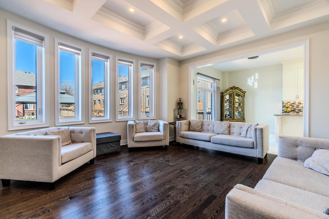 Elegant formal living room with coffered ceiling, dark hardwood floors, and floor-to-ceiling windows creating natural light.