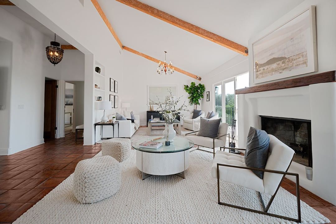 Modern living room interior with vaulted ceiling, white circular coffee table, and hardwood floors on cream area rug.