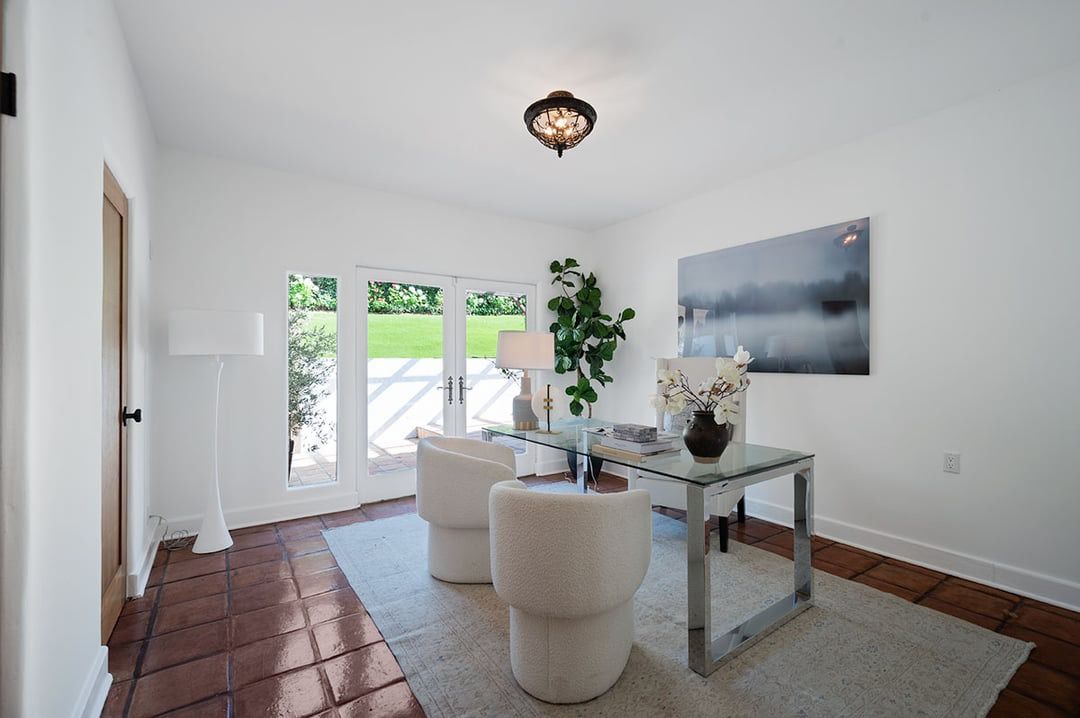 Modern dining room with white walls, terracotta tile floors, barrel chairs and glass dining table beneath hanging light fixture.